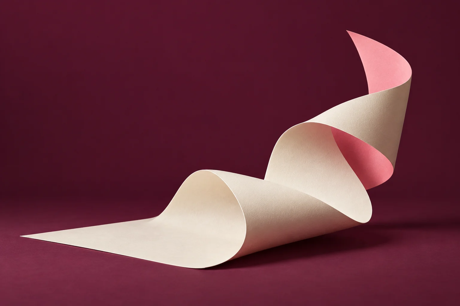 Une feuille de papier ivoire au revers rose se déploie en volume sur un fond prune